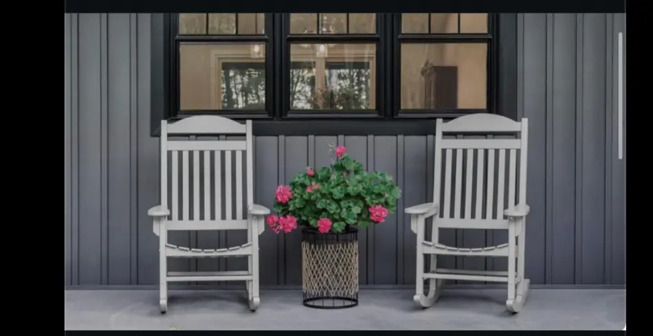 Two white wooden rocking chairs sit on a gray porch against a gray paneled wall with three black framed windows